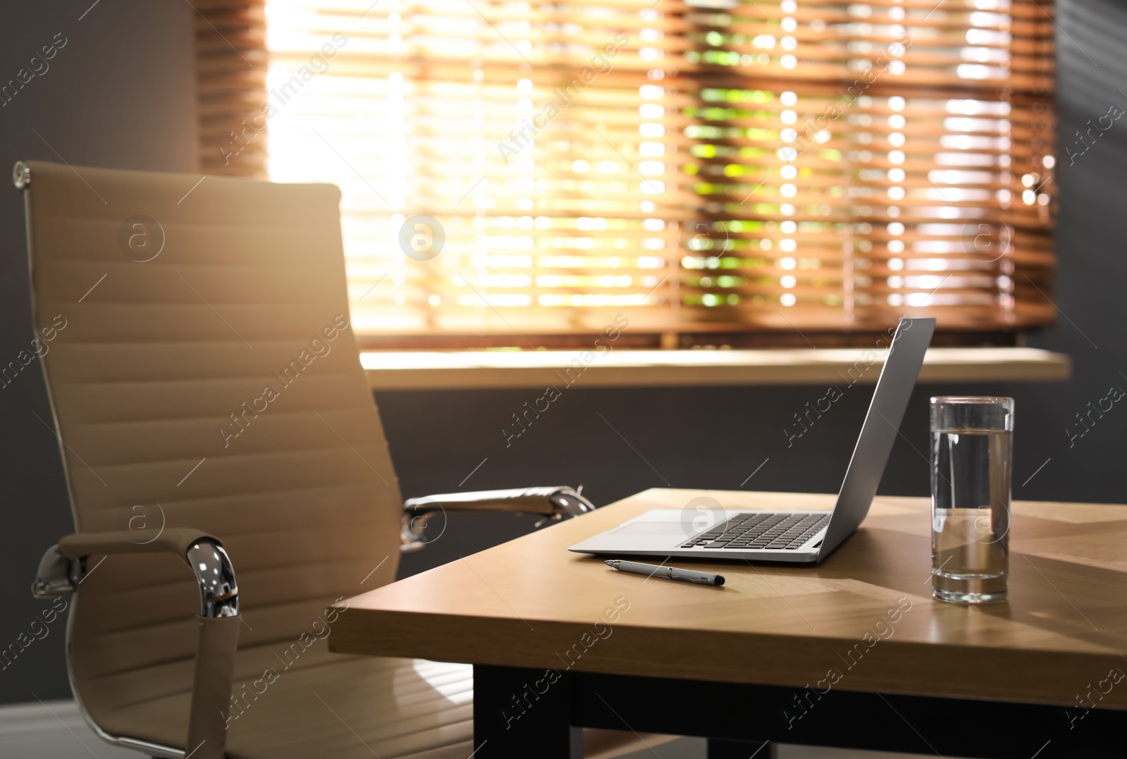 Photo of Laptop and glass of water on wooden table in modern office