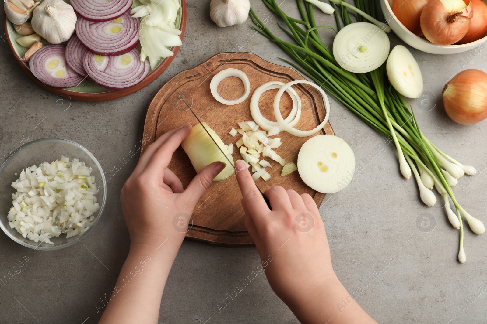 Photo of Woman cutting fresh onion on wooden board at grey table, top view