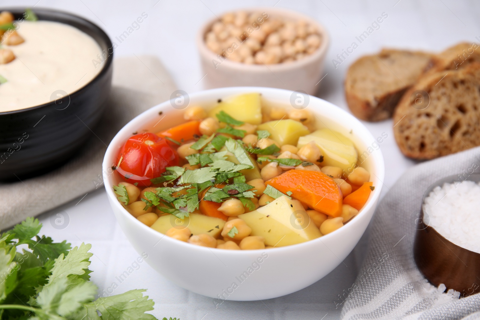 Photo of Tasty chickpea soup in bowls on white tiled table, closeup