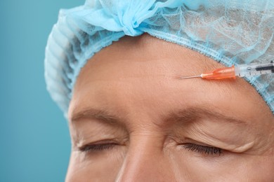 Photo of Senior woman getting facial injection on light blue background, closeup. Cosmetic surgery