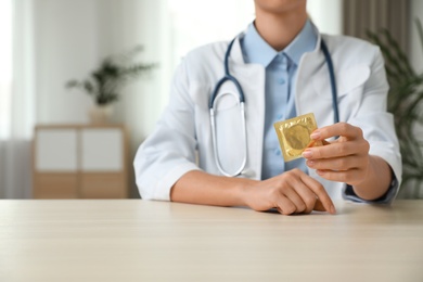 Female doctor holding condom at table indoors, closeup. Safe sex concept