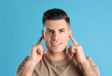 Photo of Man inserting foam ear plugs on light blue background