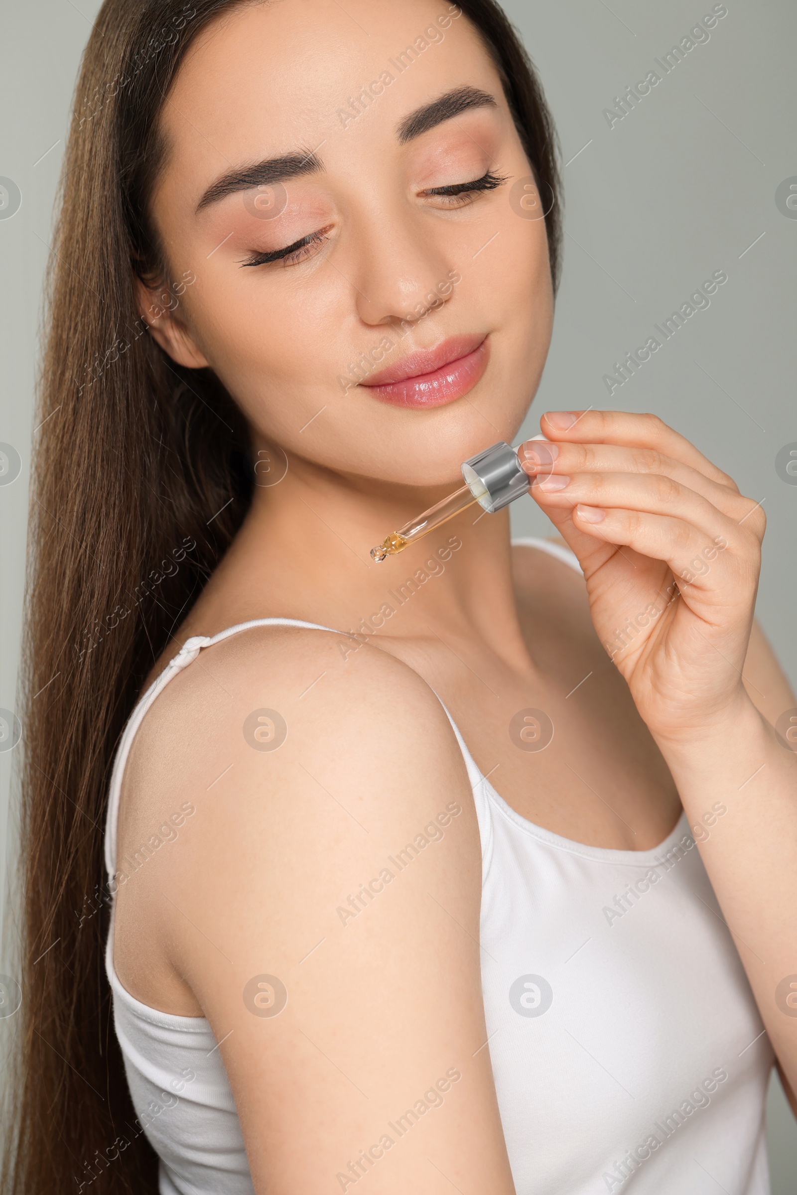 Photo of Beautiful young woman applying essential oil onto shoulder on grey background