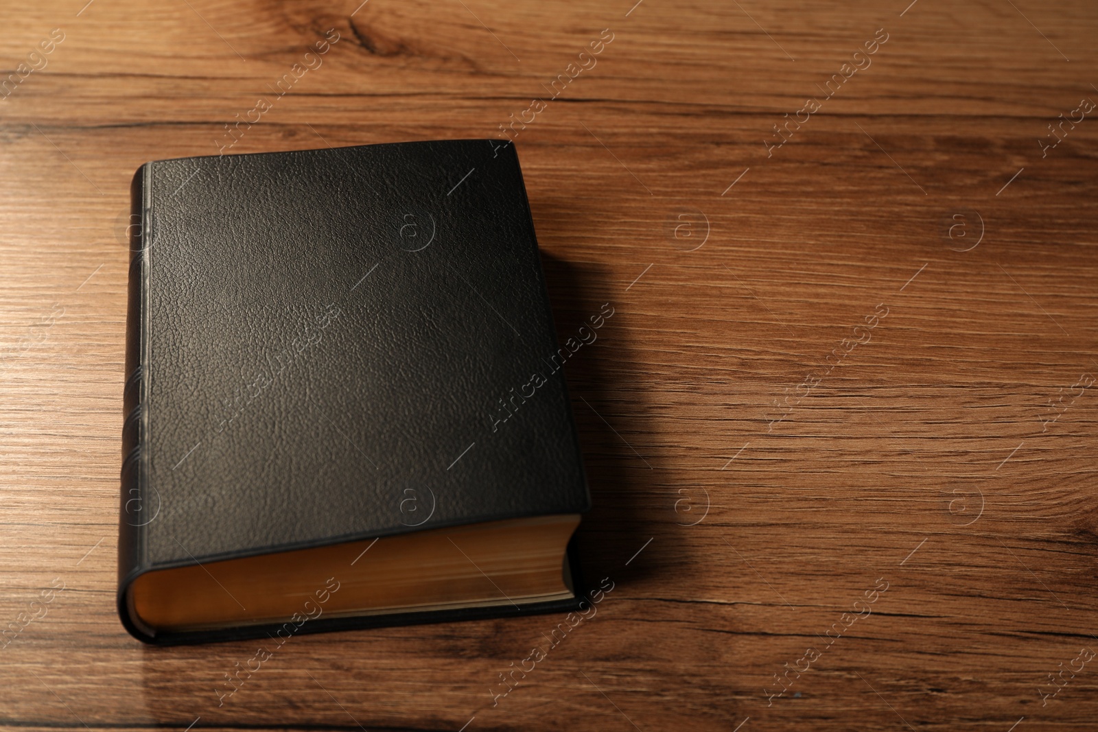 Photo of Bible with black cover on wooden table. Space for text