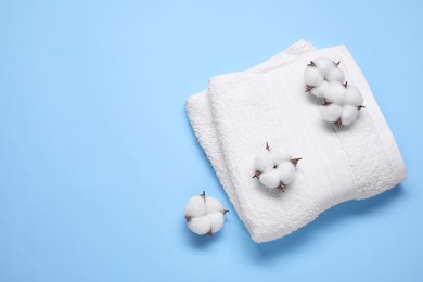 Photo of Fluffy cotton flowers and white terry towel on light blue background, top view. Space for text
