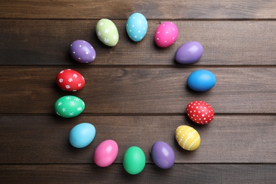 Frame of colorful eggs on wooden background, flat lay with space for text. Happy Easter