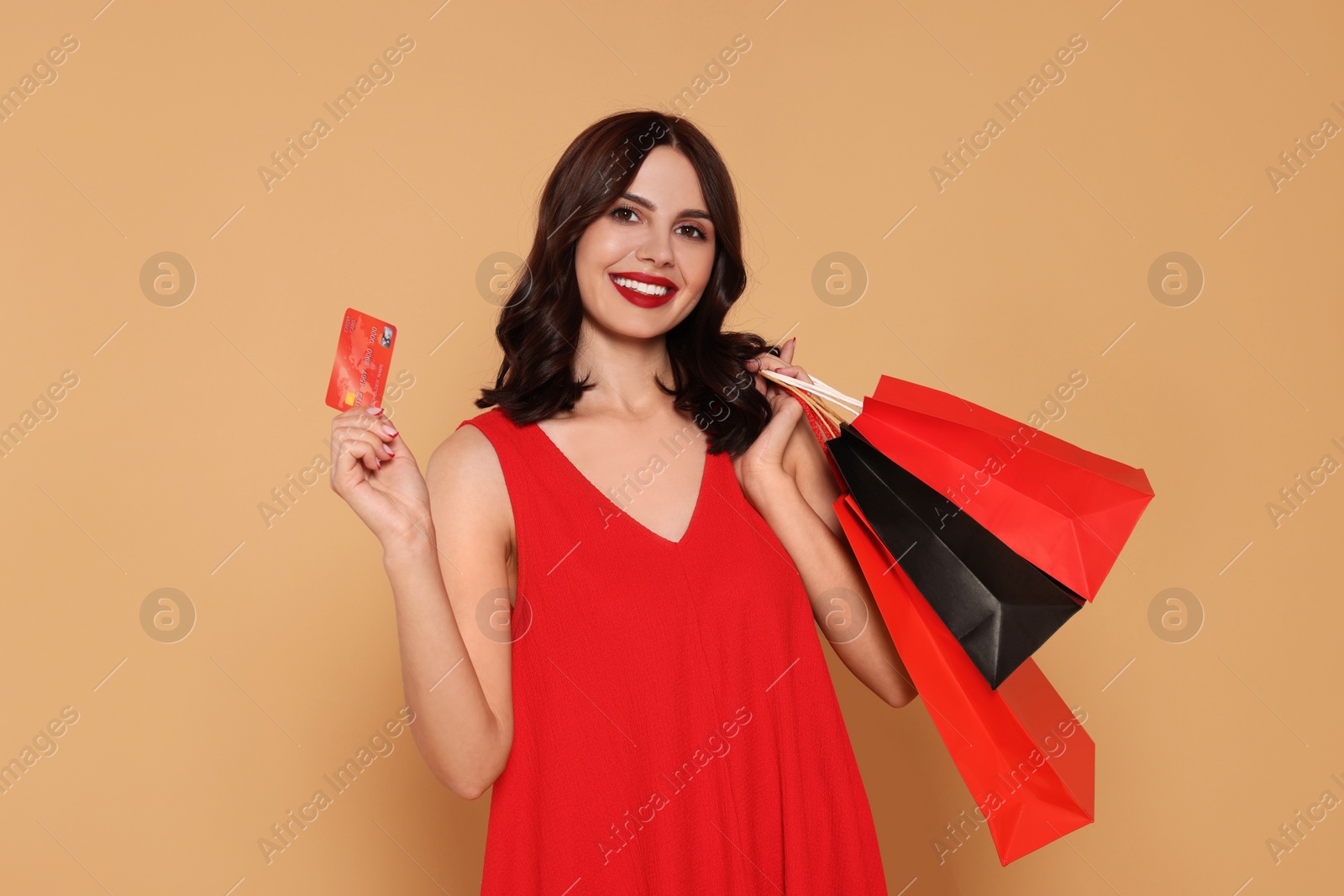 Photo of Beautiful young woman with paper shopping bags and credit card on beige background