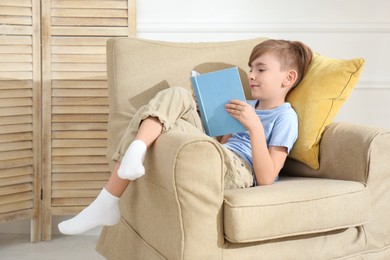 Photo of Little boy reading book in armchair at home