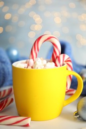 Photo of Cup of tasty cocoa with marshmallows and Christmas candy canes on white table against blurred festive lights