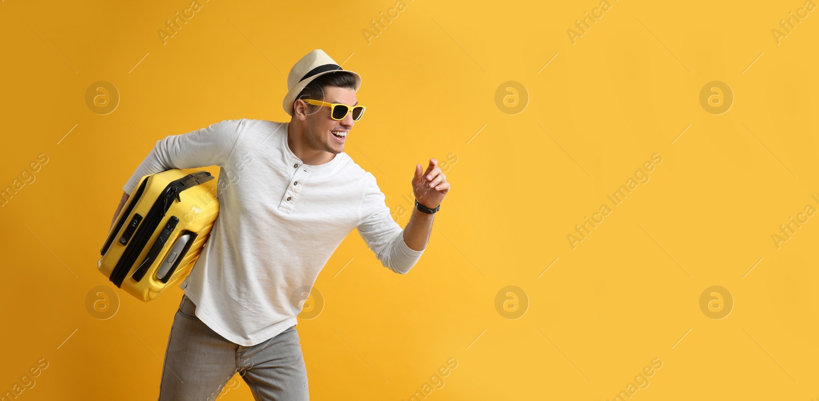 Photo of Male tourist with suitcase running on yellow background