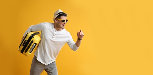 Photo of Male tourist with suitcase running on yellow background