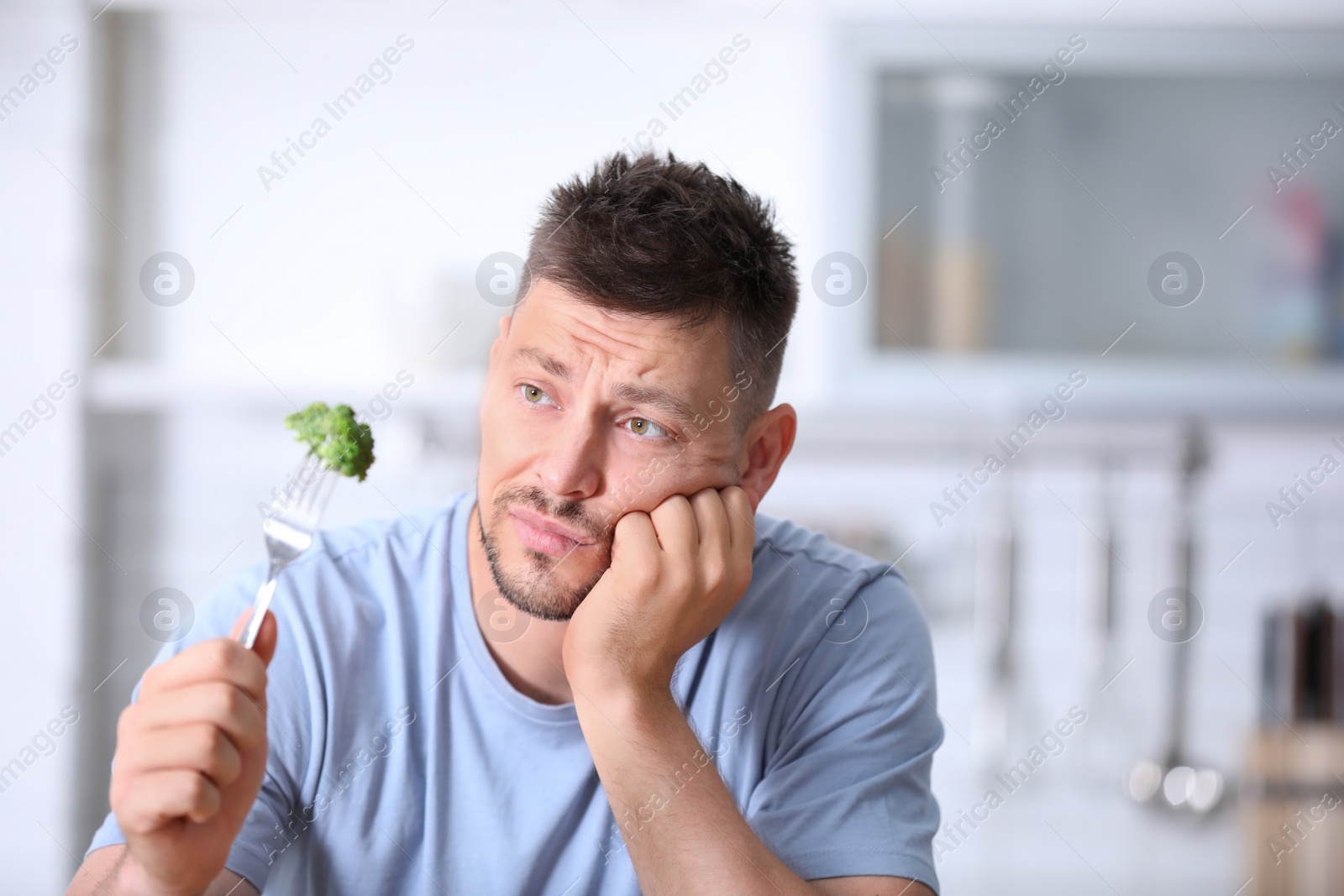 Photo of Portrait of unhappy man looking at broccoli on fork in kitchen