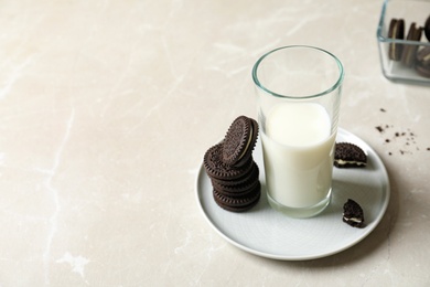 Photo of Plate with chocolate sandwich cookies and milk on grey table. Space for text