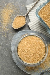 Photo of Brown sugar and spoon on grey textured table, flat lay