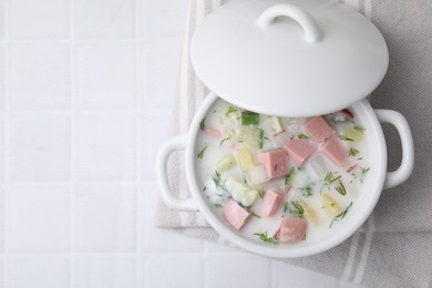 Photo of Delicious cold summer soup (okroshka) with boiled sausage in pot on white tiled table, top view. Space for text