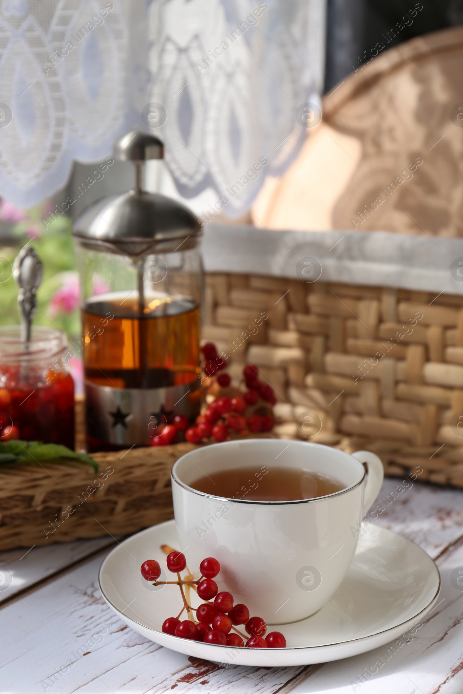 Photo of Cup of hot drink and viburnum berries on white wooden table indoors