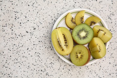 Photo of Plate of cut fresh kiwis on white table with pattern, top view. Space for text