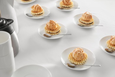 Photo of Many delicious waffles with cream served on white table for coffee break
