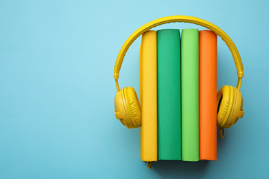 Photo of Books and modern headphones on light blue background, top view. Space for text