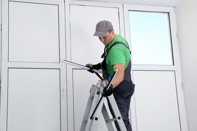 Worker on folding ladder installing window indoors