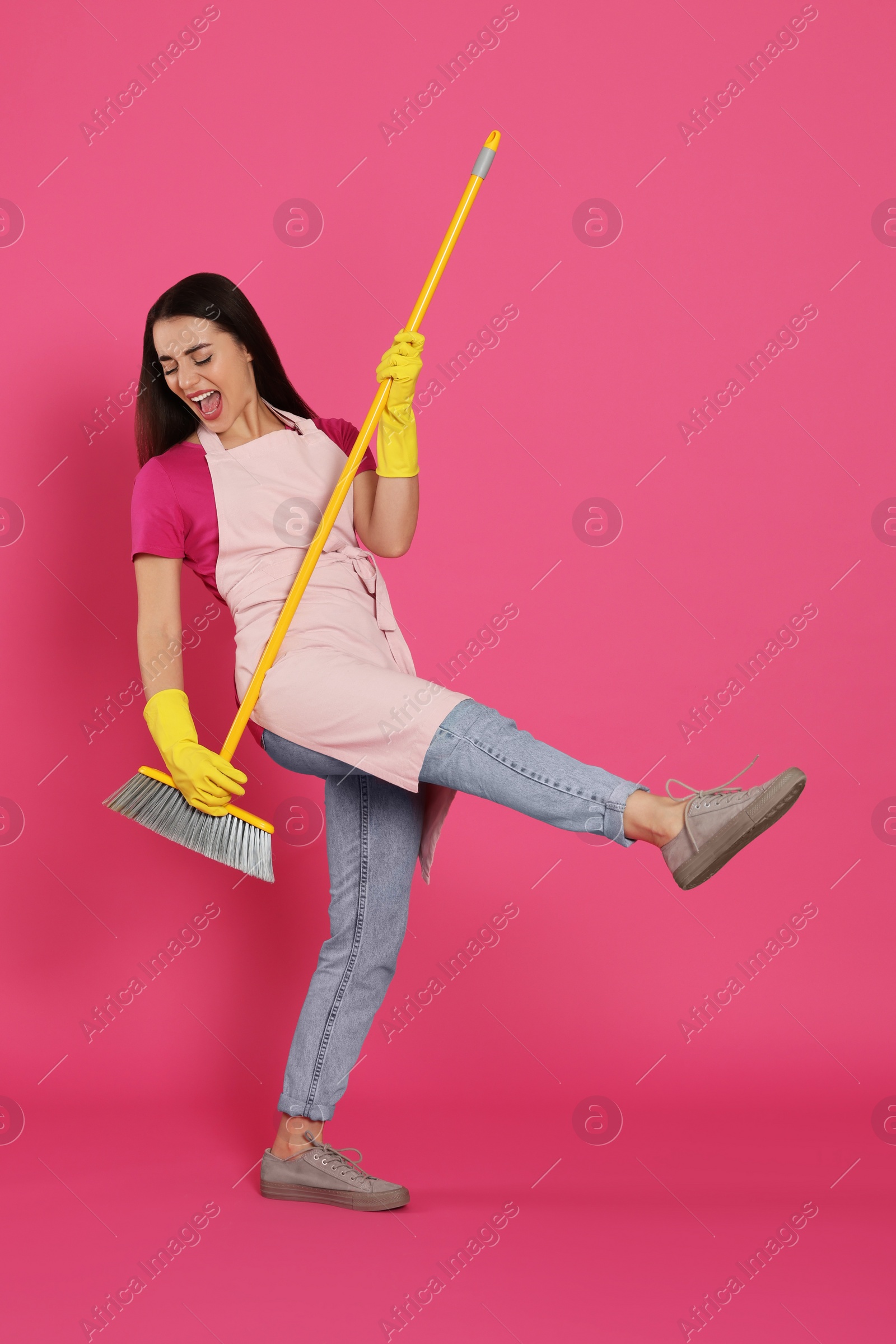 Photo of Beautiful young woman with broom singing on pink background