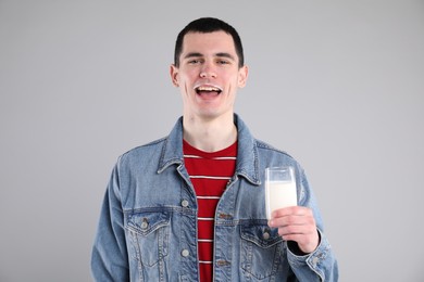 Photo of Happy man with milk mustache holding glass of tasty dairy drink on gray background