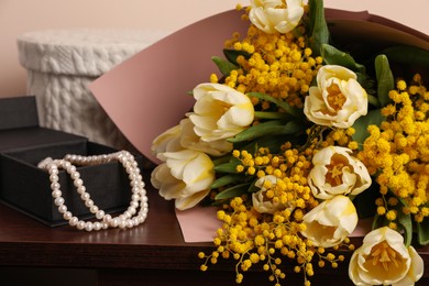 Bouquet with beautiful spring flowers and necklace on wooden chest of drawers, closeup