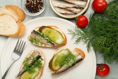 Photo of Delicious sandwiches with sprats, pickled cucumber, green onion and dill served on table, flat lay