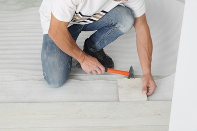 Photo of Man using hammer during installation of new laminate flooring, closeup
