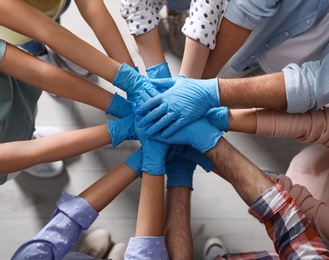 Photo of People in blue medical gloves stacking hands indoors, top view