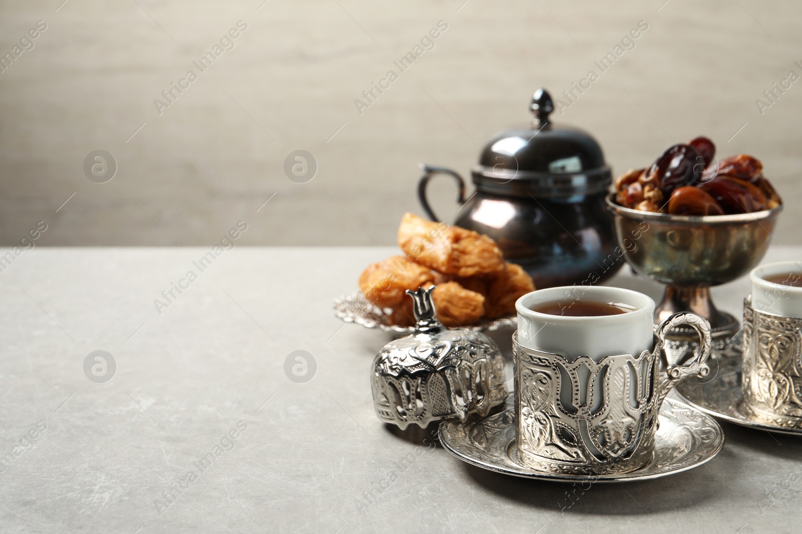 Photo of Tea, baklava dessert and date fruits served in vintage tea set on grey table, space for text