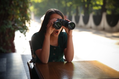 Photo of Jealous woman with binoculars spying on ex boyfriend in outdoor cafe