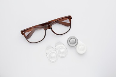Packages with contact lenses, case and glasses on white background, flat lay