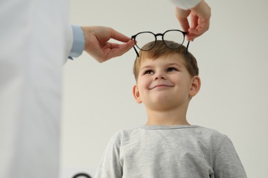 Photo of Vision testing. Ophthalmologist giving glasses to little boy indoors, low angle view