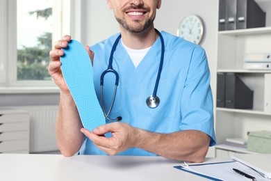 Male orthopedist showing insole in hospital, closeup