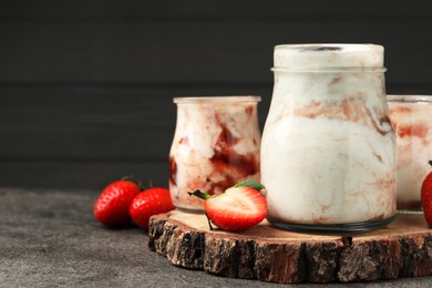 Photo of Tasty yoghurt with jam and strawberries on grey textured table, closeup. Space for text