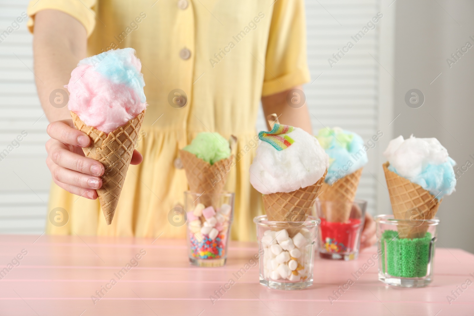 Photo of Woman holding waffle cone with cotton candy indoors, closeup