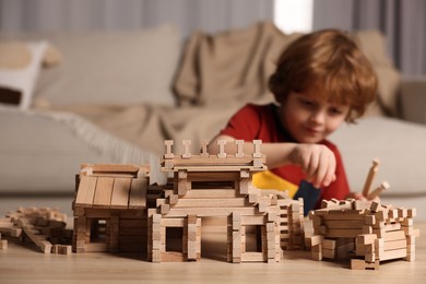 Photo of Cute little boy playing with wooden construction set at table in room, selective focus. Child's toy