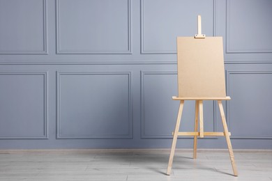 Photo of Wooden easel with blank board near grey wall indoors. Space for text