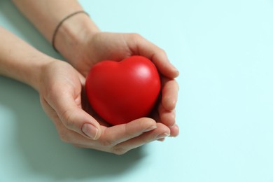 Photo of Woman holding red decorative heart on light blue background, closeup. Space for text