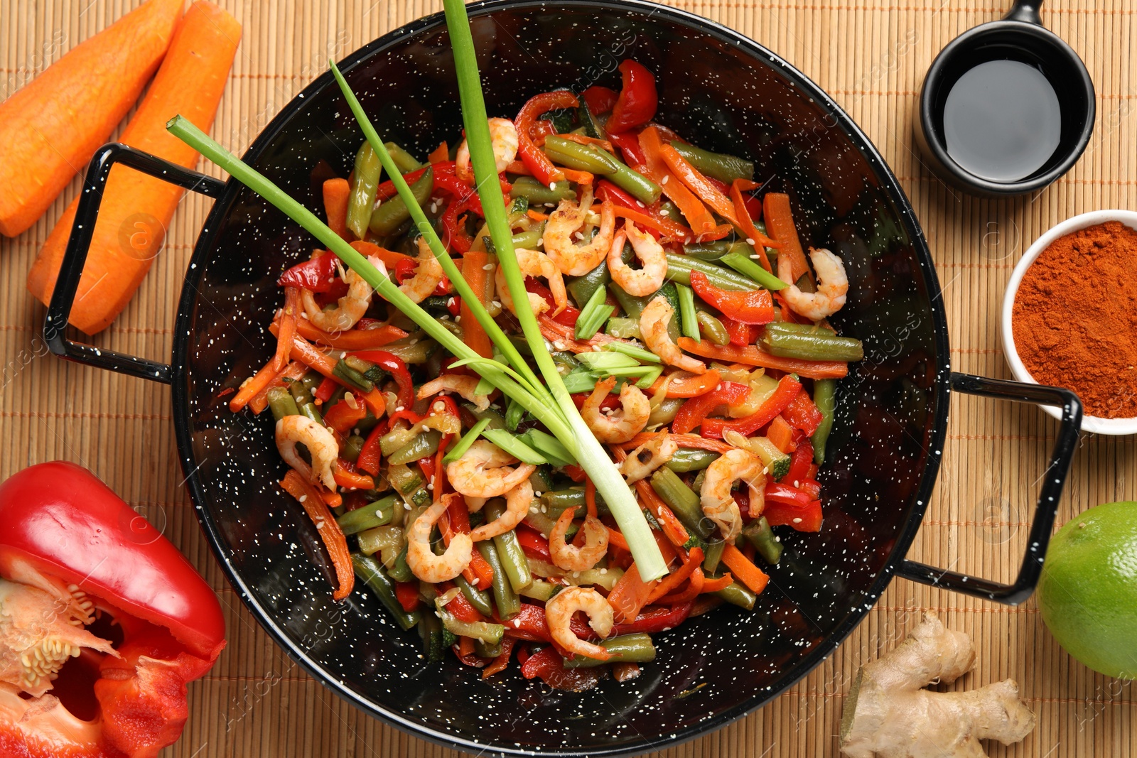 Photo of Shrimp stir fry with vegetables in wok and ingredients on table, flat lay