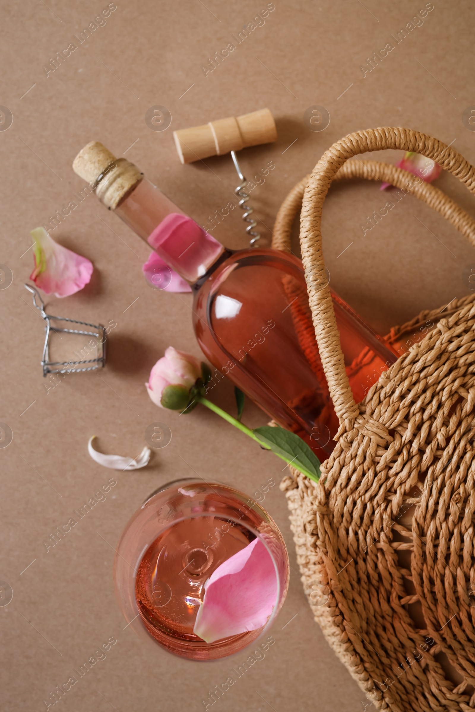 Photo of Flat lay composition with rose wine, wicker bag and beautiful pink peonies on brown background