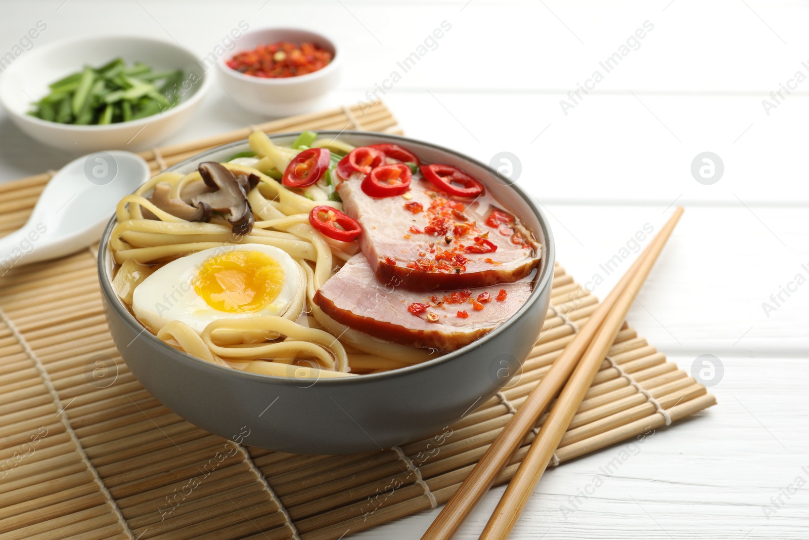 Photo of Delicious ramen in bowl and chopsticks on white wooden table, space for text. Noodle soup