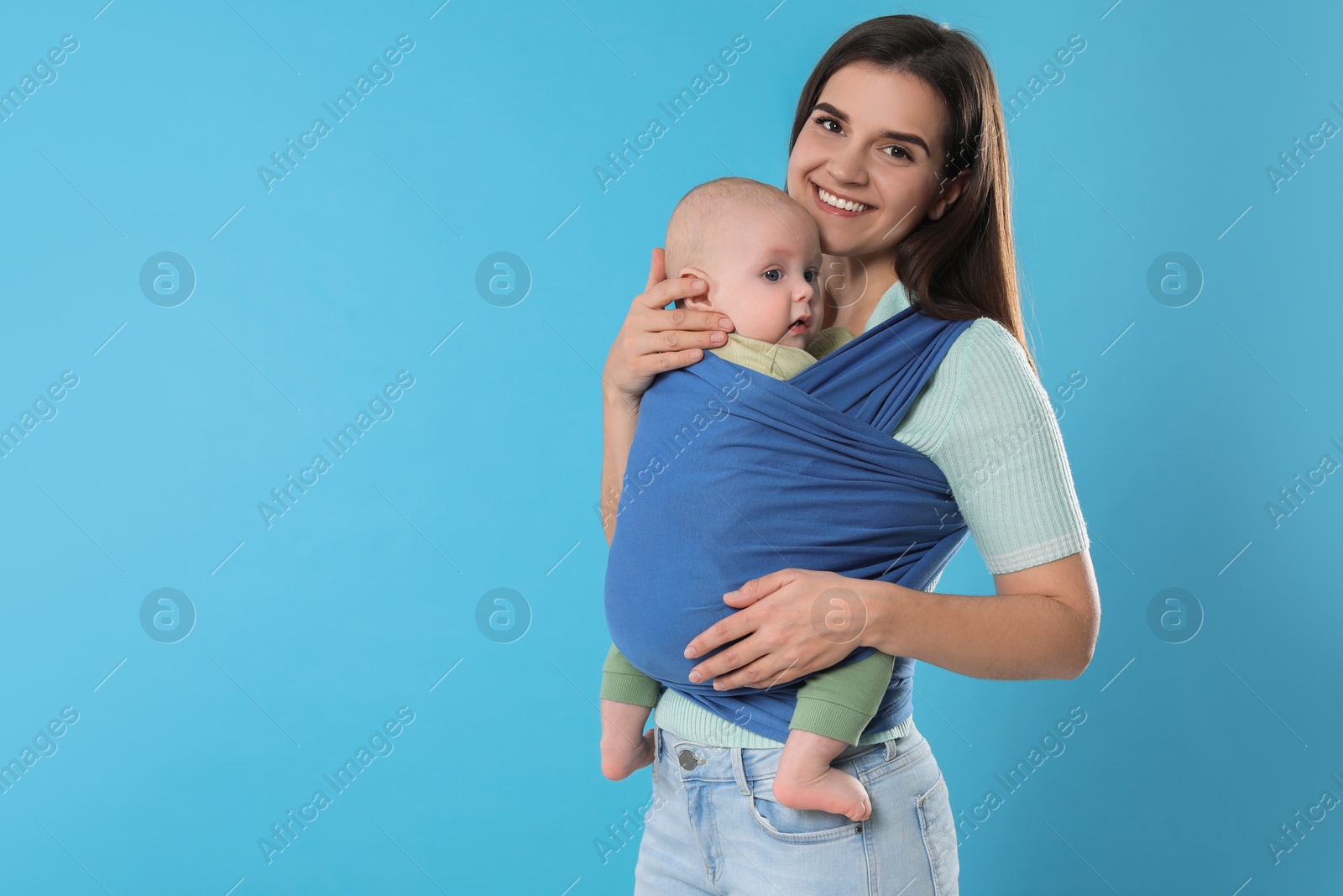 Photo of Mother holding her child in sling (baby carrier) on light blue background. Space for text