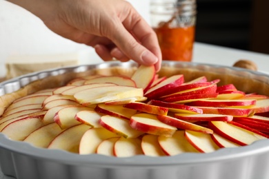 Photo of Woman putting apple slice into baking dish to make traditional English pie, closeup