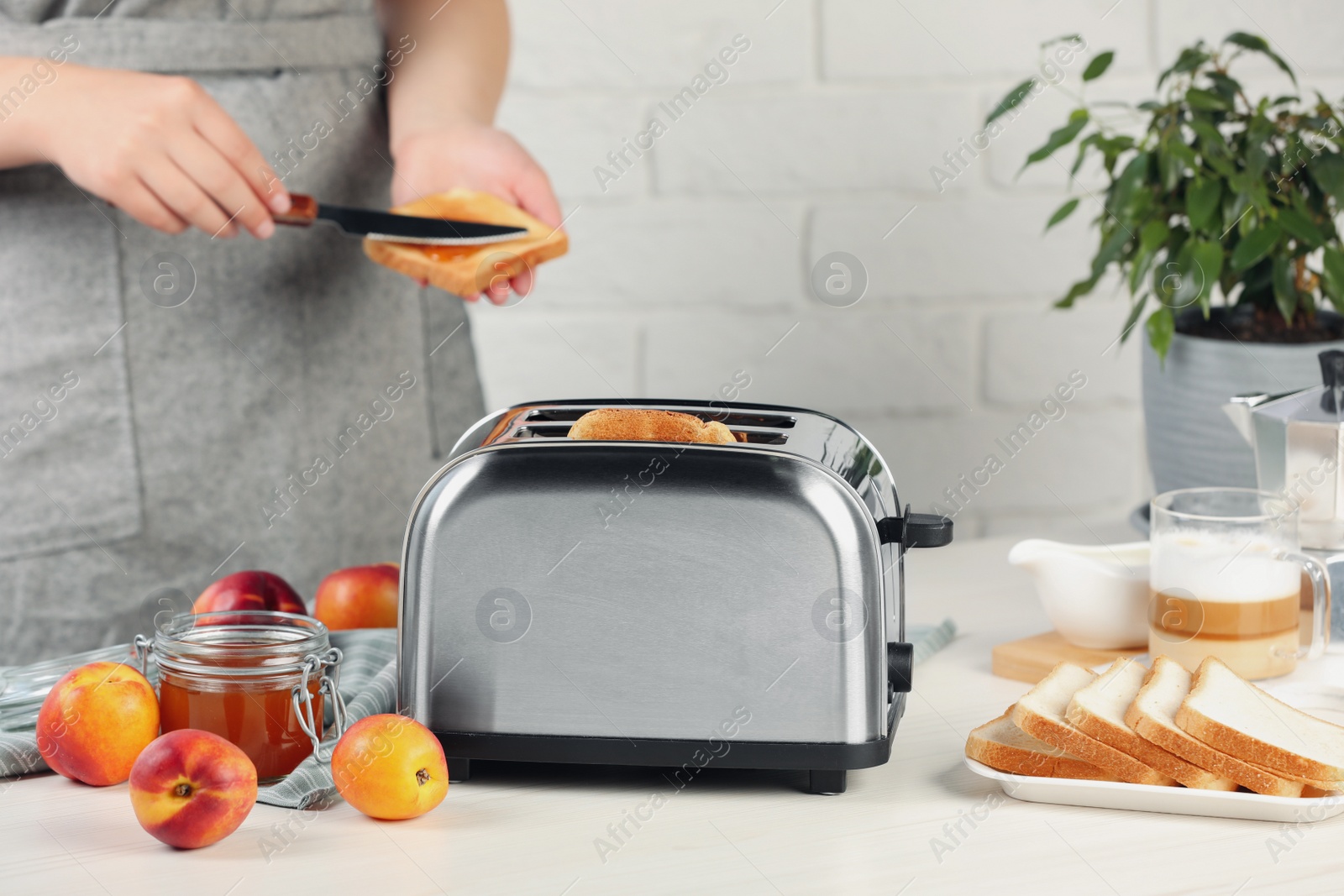 Photo of Woman spreading roasted bread with nectarine jam, closeup. Focus on modern toaster