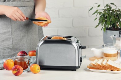 Photo of Woman spreading roasted bread with nectarine jam, closeup. Focus on modern toaster