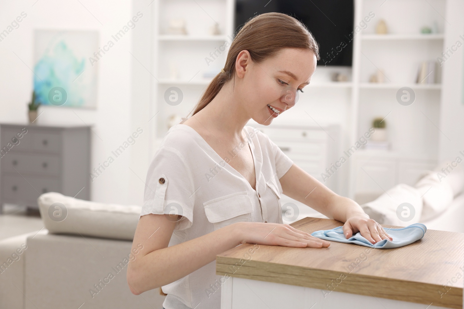 Photo of Woman with microfiber cloth cleaning wooden chest of drawers in room