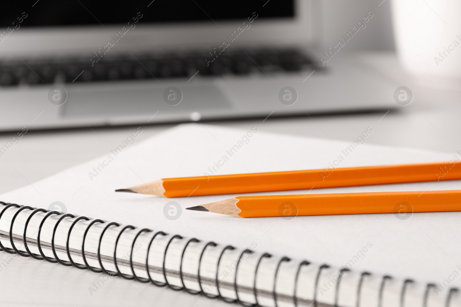 Photo of Notebook, pencils and laptop on white table, closeup