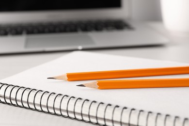 Notebook, pencils and laptop on white table, closeup